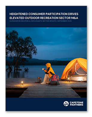 A person in a yellow jacket sits on a dock by a lake near an orange tent at dusk, embracing the tranquility and beauty offered by the outdoor recreation sector, with trees in the background and a blue sky overhead.