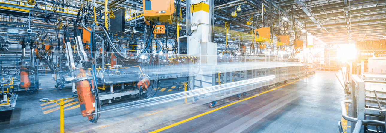 Modern industrial automotive manufacturing factory with robotic arms and machinery on an assembly line, illuminated by bright natural and artificial light.