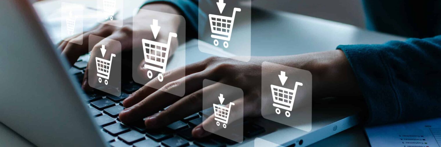 Person typing on a laptop with digital shopping cart icons overlay, representing online shopping or e-commerce activity.